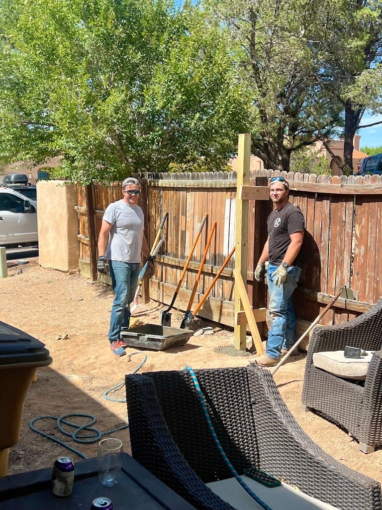 Two crew members smiling near a backyard fence with digging tools staged for post work